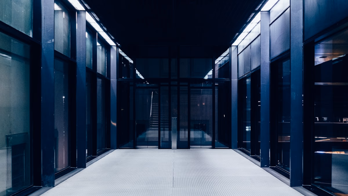 A wide-angle aerial photograph of a large data center complex surrounded by rural farmland and trees at dusk, with orange-lit server halls visible through floor-to-ceiling windows — representing the clash between AI infrastructure expansion and rural community concerns over power consumption, water use, and environmental impact.