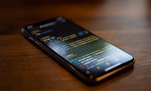 Developer using a phone to monitor a coding agent running on a laptop